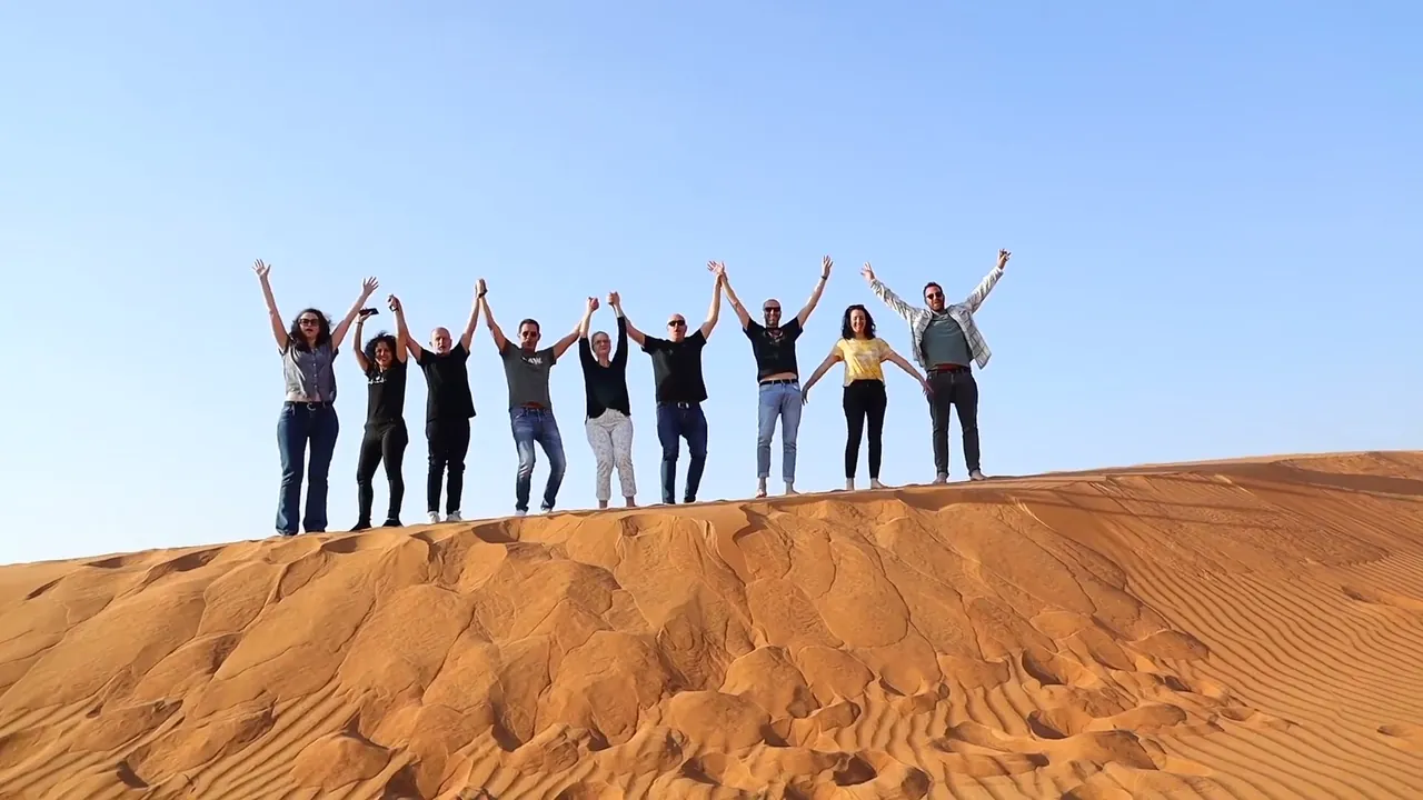 A group of guests with their arms raised on a red sand dune